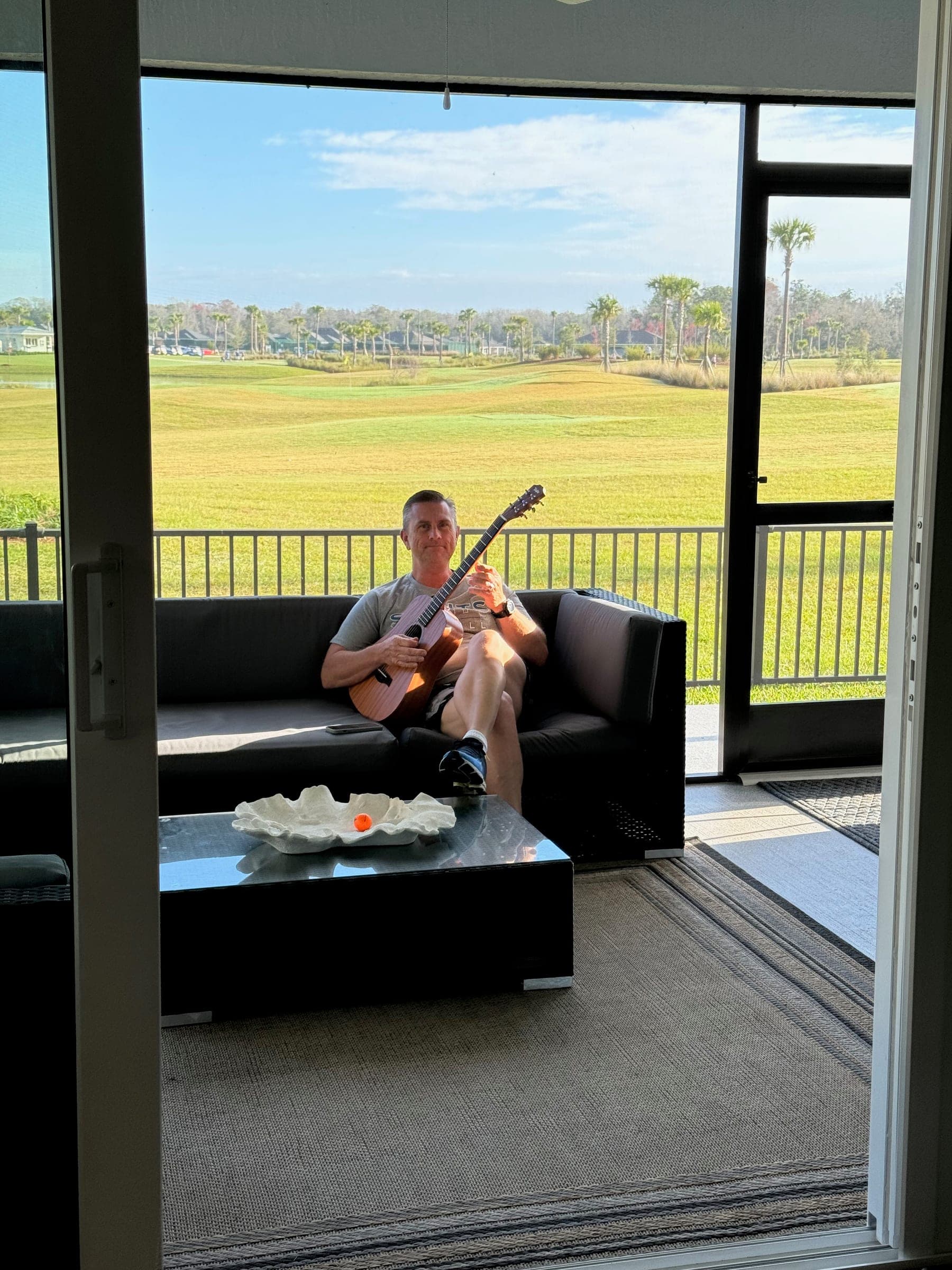 Kevin Kirk Burzynski relaxing with a guitar on a screened lanai overlooking a golf course in The Villages